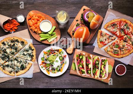 Gesunde Pflanze basiert Fast-Food-Tabelle Szene. Von oben nach unten auf einem Holzhintergrund. Pizzas aus Blumenkohlkruste, Bohnenburger, Pilztacos, Paprika nac Stockfoto