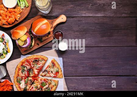 Gesunde pflanzliche Fast-Food-Seitengrenze. Blick über einen dunklen Holzhintergrund. Tischszene mit Blumenkohlkruste Pizza, Bohnenburgern und Vegetari Stockfoto