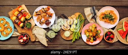 Gesunde Pflanze basierte Sommer bbq Tischszene. Ansicht von oben auf einem dunklen Holzbanner Hintergrund. Gegrilltes Obst und Gemüse, Spieße, Blumenkohlsteak A Stockfoto