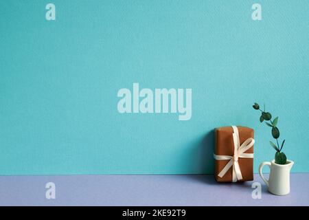 Geschenkbox und grüne Pflanze auf violettem Tisch. Blauer Hintergrund Stockfoto