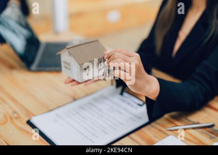 Asiatische weibliche Bankangestellte, die einem Kunden ein Haus und Schlüssel übergab, nachdem sie einen Vertrag über Papierkram unterzeichnet hatte. Stockfoto