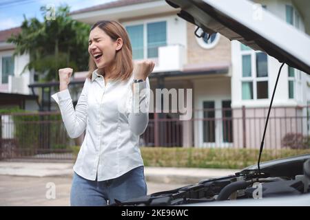 Junge verärgerte Frau, die mit geöffneter Haube in der Nähe des kaputten Autos steht. Stockfoto