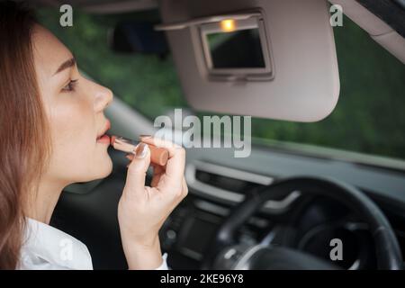 Frau, die den Rückspiegel benutzt, um sich während der Fahrt mit ihrem Auto zu schminke. Stockfoto