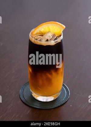 Ein Glas vereisten schwarzen amerikanischen Kaffees und eine Schicht Orange auf dem Holztisch Stockfoto