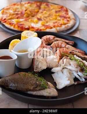 Gemischter Seafood-Teller enthält Blaukrabben, große Garnelen, Calamari-Tintenfische und gegrillten Barracuda-Fischknoblauchzehen mit Zitrone auf dem Teller Stockfoto