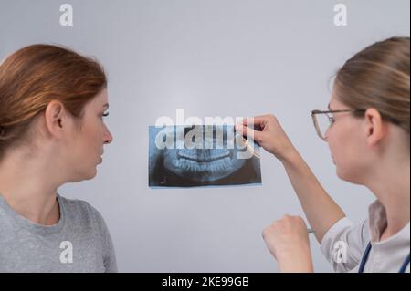 Eine Ärztin und ein Patient an der Rezeption diskutieren über eine Röntgenaufnahme des Kiefers. Stockfoto