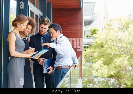 Routinearbeiten und Treffen im Freien. Eine Gruppe von Profis, die außerhalb des Büros gemeinsam ein digitales Tablet nutzen. Stockfoto