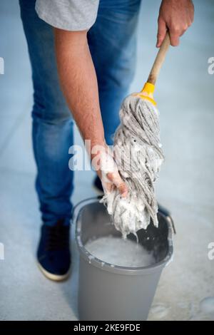 Ein nicht erkennbarer Mann klingelt einen Wischmopp aus, während er die Büroetage säubert. Stockfoto