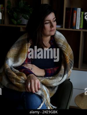 Vertikal reif nachdenklich, enttäuscht, traurig reif Brünette Frau, bedeckt von einer warmen Decke, sitzen in der Nähe Bücherregal. Burnout Stockfoto