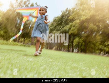 Mädchen, laufen mit Kite und Naturpark für glückliche, lustige Outdoor-Aktivitäten und Freiheit laufen im Sommer machen Kindheitserinnerungen. Verspieltes Kind, Grasfeld Stockfoto