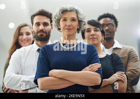 Wir stehen stark, wenn wir zusammenstehen: Eine vielfältige Gruppe von Geschäftsleuten, die mit gekreuzten Armen im Büro stehen. Stockfoto