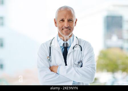 Ich hatte immer eine Leidenschaft, anderen zu helfen. Ein reifer männlicher Arzt stand mit gekreuzten Armen. Stockfoto