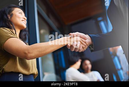 Im Glad weve erzielte eine Einigung. Zwei Geschäftsleute schüttelten sich mit ihren Mitarbeitern im Hintergrund die Hände. Stockfoto