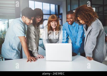 Dieser Laptop bedeutet Geschäft. Eine Gruppe junger Geschäftsleute drängte sich in ihrem Büro um einen Laptop. Stockfoto