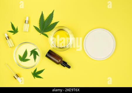 Natürliches Hanföl. Zusammensetzung von Cannabisölflaschen und Hanfblättern auf gelbem Hintergrund, Nachbildung, flach liegend. Stockfoto