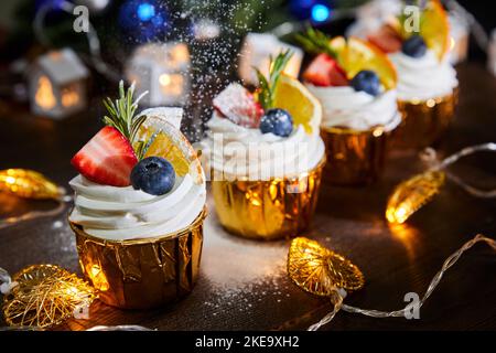 Weihnachtskuchenkuchen mit frischen Blaubeeren und Erdbeeren auf einem Hintergrund glühender Girlanden Stockfoto