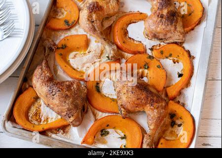 Gebratene Hähnchenschenkel mit Kürbis auf einem Backblech Stockfoto