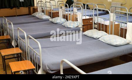 Soldatenbetten in der Kaserne. Eine Reihe von Betten gemacht russischen Armee, das wirkliche Leben. Stockfoto