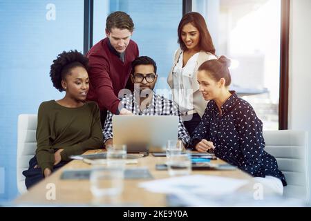 Jeder bekommt Input für das beste Ergebnis. Eine Gruppe von Designern diskutiert etwas auf einem Laptop im Sitzungssaal. Stockfoto