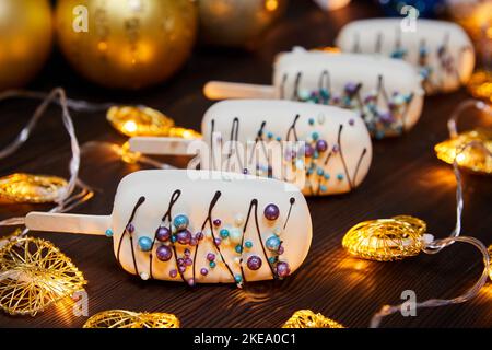 Weisses weihnachtliches Dessert in Form von Mousse auf einem Stock auf einem Hintergrund glühender Girlanden Stockfoto