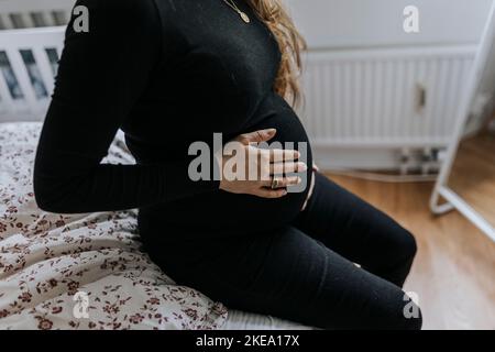 Eine Schwangerin sitzt auf dem Bett und berührt den Bauch Stockfoto