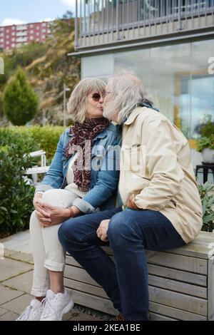 Seniorenpaar sitzt auf der Bank und küsst sich Stockfoto