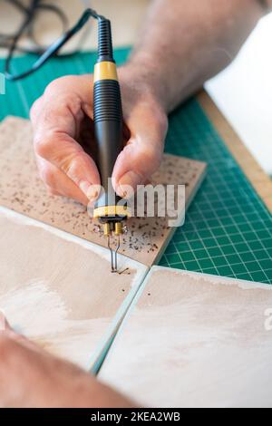 Nahaufnahme Mann, der mit dem Pyrografen arbeitet, der die Holzherstellung in seinem Atelier verbrennt. Stockfoto