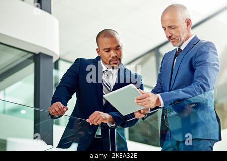 Lassen Sie mich Ihnen diese E-Mail zeigen, über die ich gesprochen habe: Ein Geschäftsmann, der seinem Kollegen auf seinem Tablet im Büro etwas vorführt. Stockfoto
