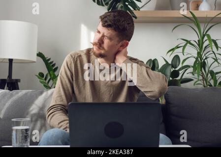Müde unwell Kerl überwältigt von Computer-Arbeit sitzende Lebensweise Kampf mit Rückenschmerzen oder Schmerzen. Erschöpfter junger bärtiger Mann, der auf der Couch sitzt Stockfoto