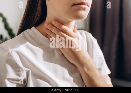 Eine kurze Aufnahme einer Frau, die unter Schmerzen leidet und zu Hause auf dem Sofa sitzt. Gesundheitswesen und medizinisches Konzept. Ungesunde traurige junge kaukasische Frau mit wund thro Stockfoto