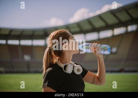 Eine atemberaubende blonde Läuferin trinkt Wasser und nimmt nach dem Laufen eine Pause ein Stockfoto