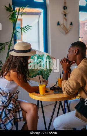 Zwei schöne multirassische Touristen reden über das nächste Reiseziel. Sie sitzen in einer Kaffeebar Stockfoto