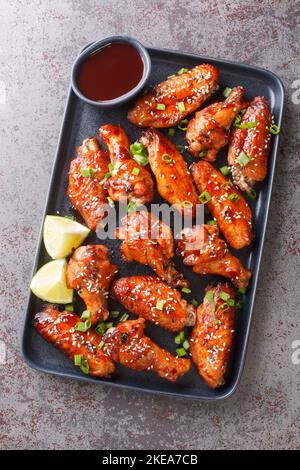 Fast Food gebratene Sticky Hoisin Wings Nahaufnahme auf dem Teller auf dem Tisch. Vertikale Draufsicht von oben Stockfoto