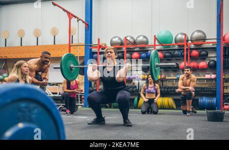 Frau Gewichtheben, während ihre Gym-Kollegen sie anfeuern Stockfoto