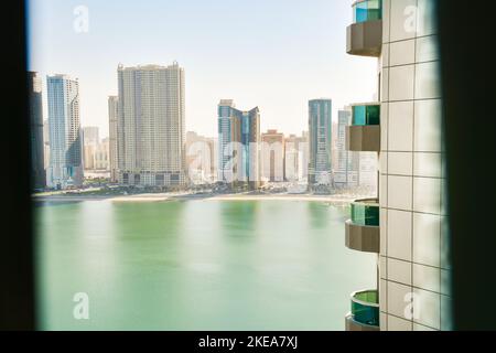 Panoramafenster mit Blick auf hohe Gebäude mit Balkon und Yachthafen im Sharjah-Viertel. Mietwohnung atemberaubende Aussicht und Immobiliengeschäft in uni Stockfoto