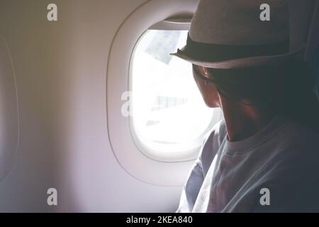 Frau schaut aus dem Fenster eines fliegenden Flugzeuges. Junge Passagiere reisen mit dem Flugzeug und beobachten den Himmel von oben Stockfoto