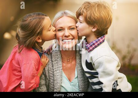 Duschende Mutter mit etwas Liebe. Porträt einer Mutter, die von ihren beiden Kindern auf beiden Seiten ihrer Wangen geküsst wird. Stockfoto