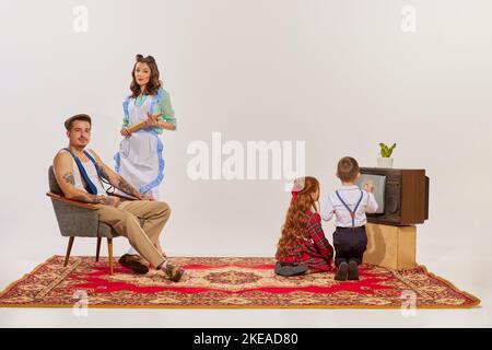 Porträt einer jungen Familie, die isoliert auf grauem Hintergrund Fernsehen sieht. Kinder sehen sich Cartoons an. Stockfoto