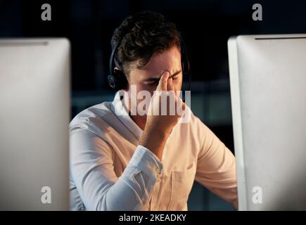 Callcenter, Telemarketing und ein Mann mit Kopfschmerzen und Stress, der nachts Überstunden macht. Burnout, müder und frustrierter männlicher Berater, der im Büro sitzt Stockfoto
