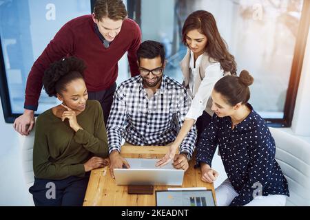 Eine Gruppe von Designern, die auf einem Laptop im Sitzungssaal über etwas diskutieren. Stockfoto