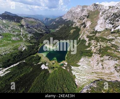 Luftaufnahme des herzförmigen Sees im Trnovacko See in Montenegro. See umgeben von Bergen mit Schnee. Wanderleben. Reisen und Abenteuer Stockfoto