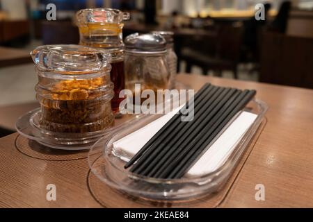 Nahaufnahme der verschiedenen Arten von Gewürzen, Essstäbchen und Taschentücher auf dem Restauranttisch zur Selbstbedienung. Stockfoto