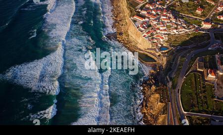 Luftdrohnenaufnahme von Azenhas do Mar, Portugal. Natürlicher Pool im Meer, neben der Klippe und einem Dorf am Meer während des Sonnenuntergangs. Beste Reiseziele. Stockfoto