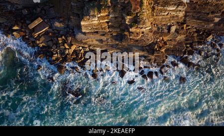 Luftdrohnen-Ansicht von Meereswellen, die während des Sonnenuntergangs gegen die Felsen einer Klippe krachen. Reisen und Urlaub. Entspannende Momente. Stockfoto