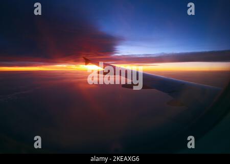Wunderschöner Sonnenaufgang am Himmel während des Fluges. Flugzeug Flügel über dem bewölkten bunten Sonnenuntergang Stockfoto