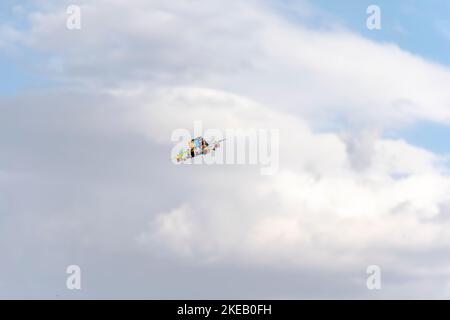 Fliegende Quadcopter-Drohne mit blauem wolkigen Himmel im Hintergrund. Flachsicht des mehrfarbigen, nicht manierten Fahrzeugs in der Luft. Stockfoto