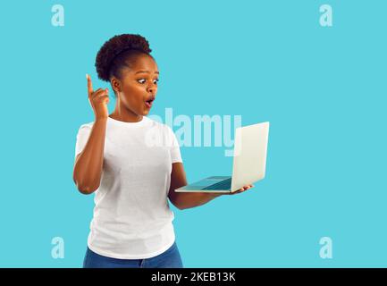 Überrascht afroamerikanische Frau, die eine Idee hatte, den Bildschirm des Laptops auf blauem Hintergrund zu betrachten. Stockfoto