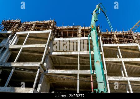 Betonplatten auf einer Baustelle gießen, mit Kränen und Gießrohren, unbekannte Arbeiter auf dem Dach des Stahlbetons. Stockfoto