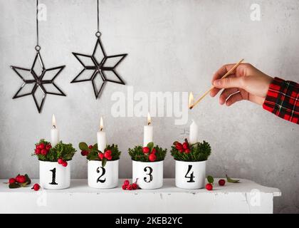 Mädchen zündet die vierte Kerze auf einem handgefertigten Adventskranz an, der mit roten Schachbrettbeeren verziert ist. Weihnachtsdekoration Konzept. Speicherplatz kopieren. Stockfoto