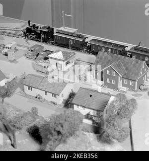 In der 1950s. Eine Modelleisenbahn, die auf einem Tisch in einem Kinderzimmer montiert ist. Die Modelleisenbahn hat Häuser, Bäume, Tiere und Menschen in ihr als maßstabsgetrete Modelle. Höchstwahrscheinlich ein Zugsatz des deutschen Herstellers Fleischmann, da die Schienen das typische zweigleisige Gleichstrom-System sind. Ein maßstabsgezeichtes Modell eines abendlichen Nachrichtenwagens mit einem Schild auf der Oberseite, das zuerst mit den Nachrichten sagte. Schweden 1958. Conard Ref. 3867 Stockfoto